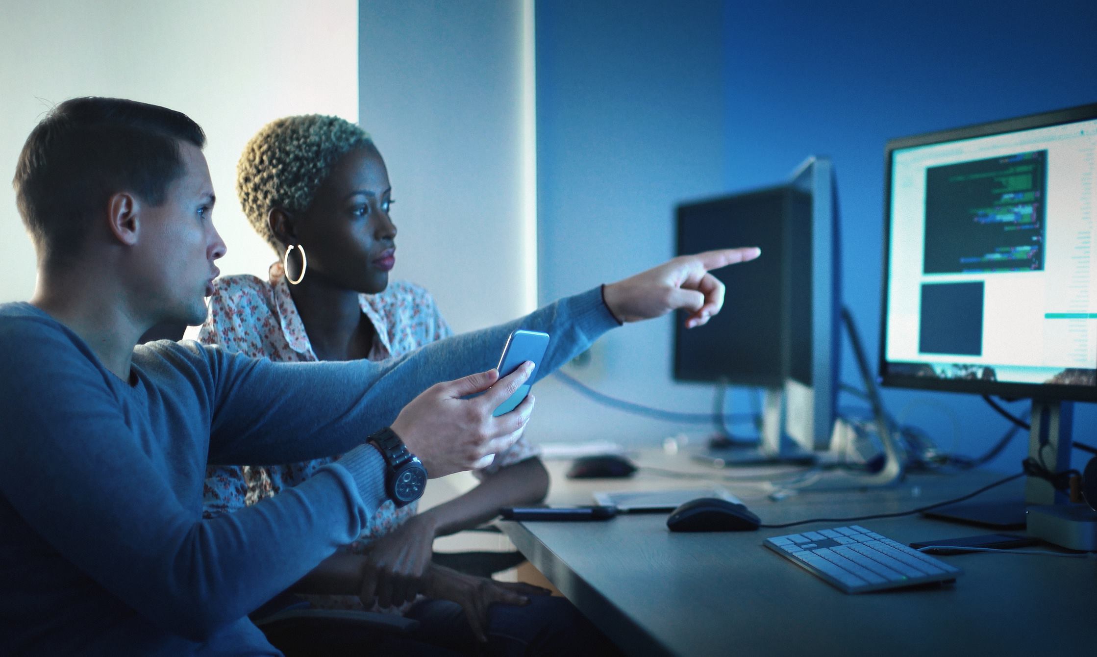 A man and woman working together and pointing at a computer, in an office. 